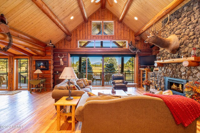 living room featuring a stone fireplace, rustic walls, high vaulted ceiling, light hardwood / wood-style flooring, and beam ceiling