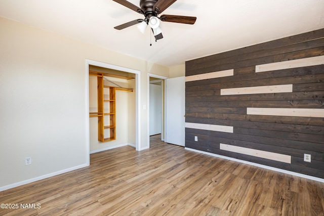 unfurnished room featuring ceiling fan, wooden walls, baseboards, and wood finished floors