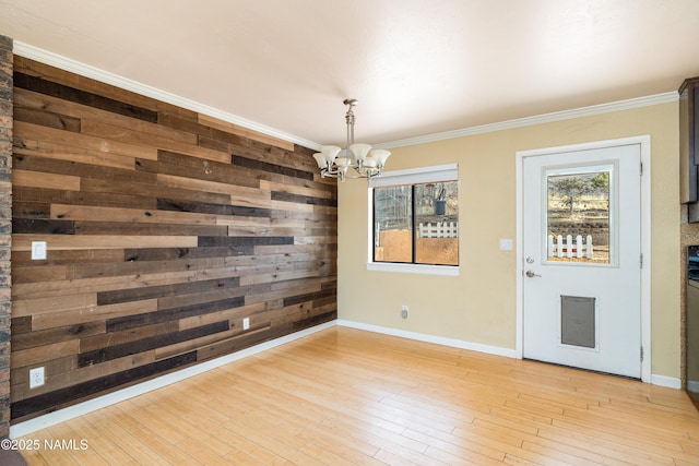 unfurnished dining area with crown molding, a notable chandelier, light wood-style flooring, and baseboards