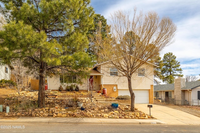 split level home featuring a garage, concrete driveway, brick siding, and fence