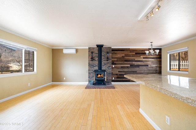 unfurnished living room featuring a wall mounted air conditioner, a wood stove, crown molding, light wood-type flooring, and wood walls