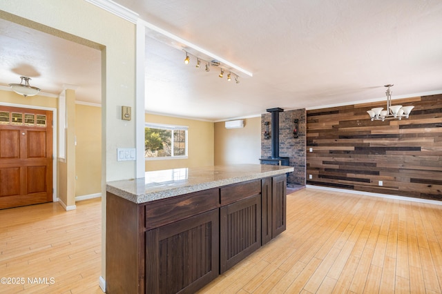 kitchen with crown molding, a wood stove, wood walls, and light wood finished floors