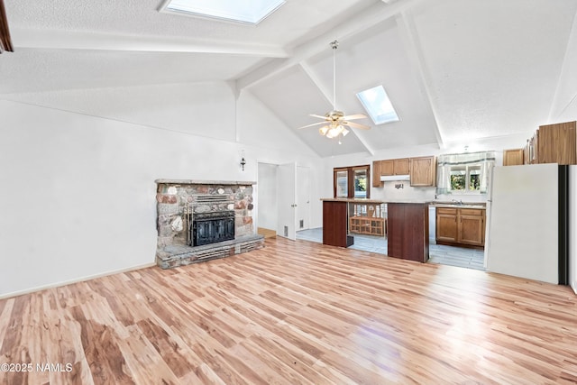 unfurnished living room with light hardwood / wood-style flooring, ceiling fan, beam ceiling, a skylight, and a stone fireplace