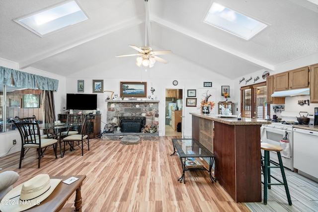 kitchen featuring white appliances, ceiling fan, vaulted ceiling with skylight, a fireplace, and light wood-type flooring