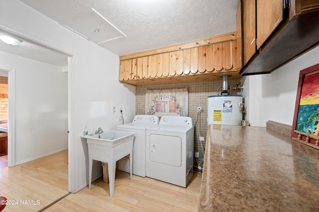 washroom featuring washing machine and dryer, water heater, a textured ceiling, and light wood-type flooring