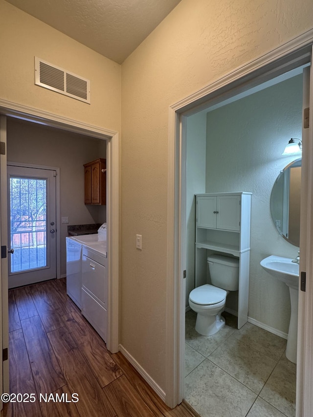 clothes washing area with a textured ceiling, light hardwood / wood-style flooring, cabinets, and washing machine and clothes dryer