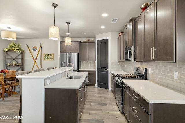 kitchen featuring appliances with stainless steel finishes, decorative light fixtures, decorative backsplash, sink, and a kitchen island with sink