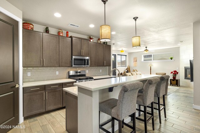 kitchen with a kitchen breakfast bar, dark brown cabinets, hanging light fixtures, appliances with stainless steel finishes, and a kitchen island with sink