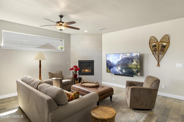 living room featuring a tiled fireplace and ceiling fan