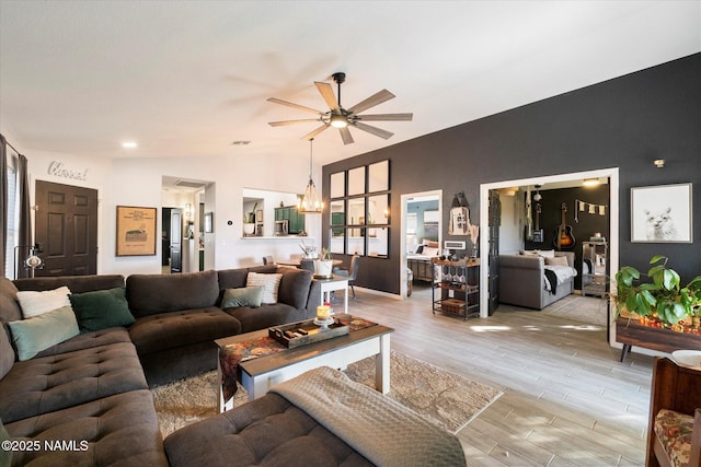 living room with ceiling fan with notable chandelier, light hardwood / wood-style flooring, and lofted ceiling