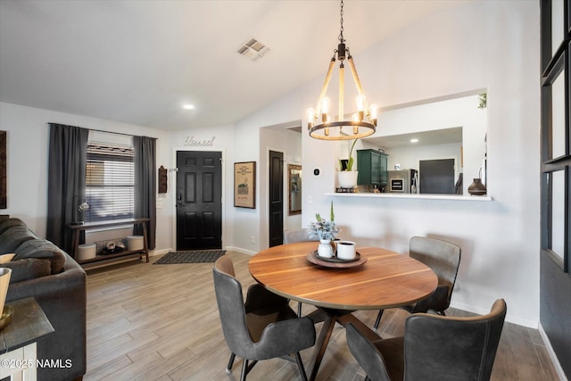 dining space featuring light wood-type flooring, a notable chandelier, and lofted ceiling