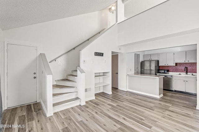 kitchen featuring a textured ceiling, stainless steel appliances, tasteful backsplash, sink, and high vaulted ceiling