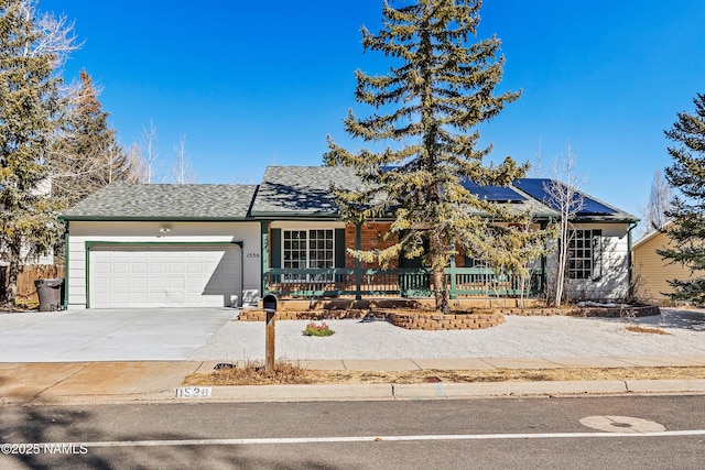 ranch-style home featuring an attached garage, driveway, a shingled roof, and solar panels