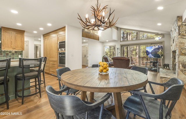 dining room featuring french doors, a fireplace, a notable chandelier, light hardwood / wood-style floors, and lofted ceiling