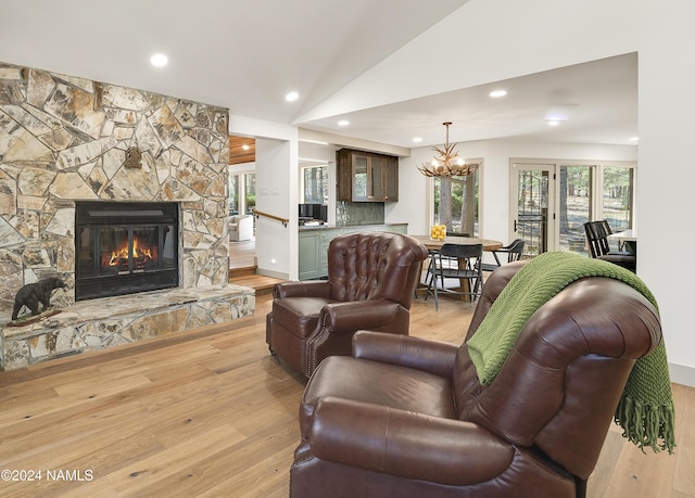 living room featuring an inviting chandelier, light hardwood / wood-style flooring, lofted ceiling, and a fireplace