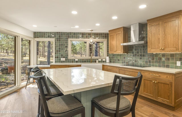 kitchen featuring a center island, black electric stovetop, wall chimney range hood, sink, and light hardwood / wood-style flooring