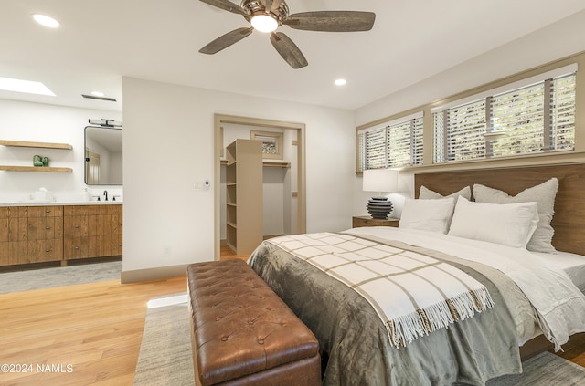 bedroom with a walk in closet, a skylight, light wood-type flooring, a closet, and ceiling fan