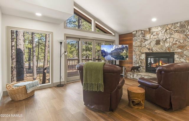 living room with wood-type flooring, lofted ceiling, a stone fireplace, and french doors