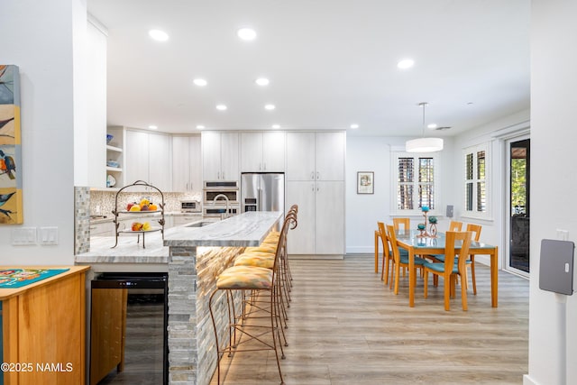 kitchen featuring white cabinetry, kitchen peninsula, stainless steel appliances, wine cooler, and a breakfast bar area