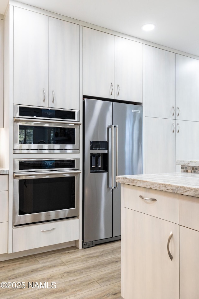 kitchen with white cabinets, light hardwood / wood-style floors, stainless steel appliances, and light stone counters