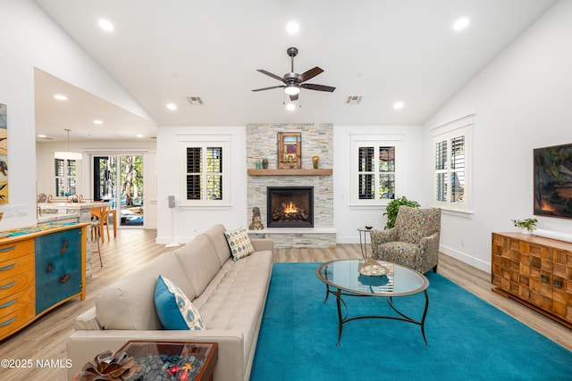 living room with hardwood / wood-style flooring, ceiling fan, a stone fireplace, and lofted ceiling