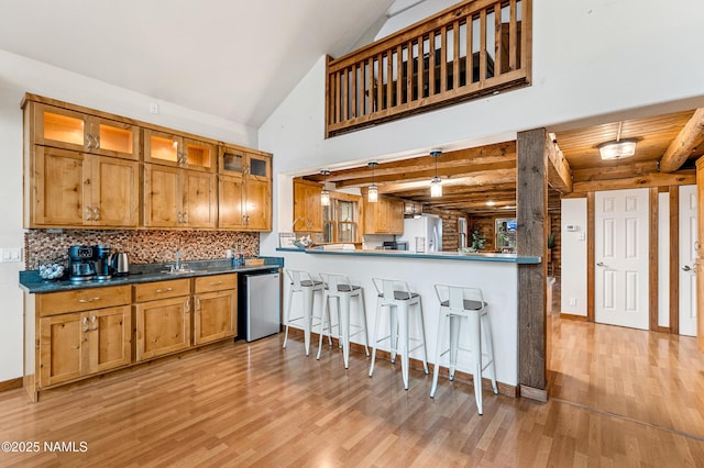 kitchen featuring dishwasher, a breakfast bar area, brown cabinetry, light wood-style flooring, and backsplash