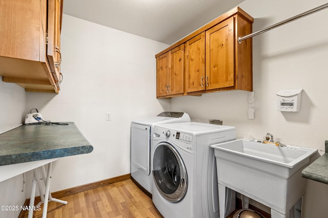washroom with light wood-style floors, baseboards, a sink, cabinet space, and independent washer and dryer
