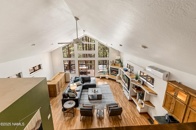 living room featuring a lit fireplace, a ceiling fan, a textured ceiling, light wood-type flooring, and lofted ceiling