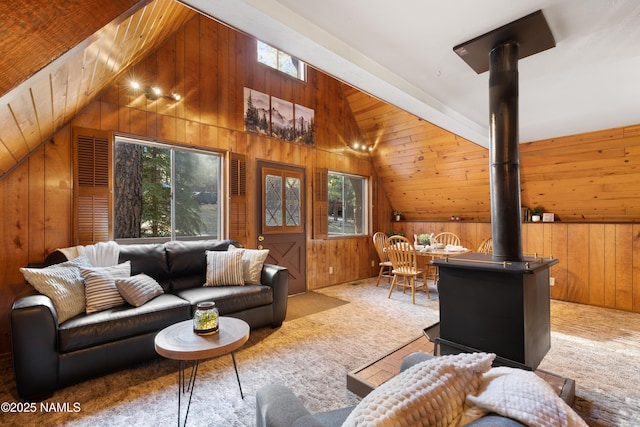 living room featuring lofted ceiling, wood walls, a wood stove, and a healthy amount of sunlight
