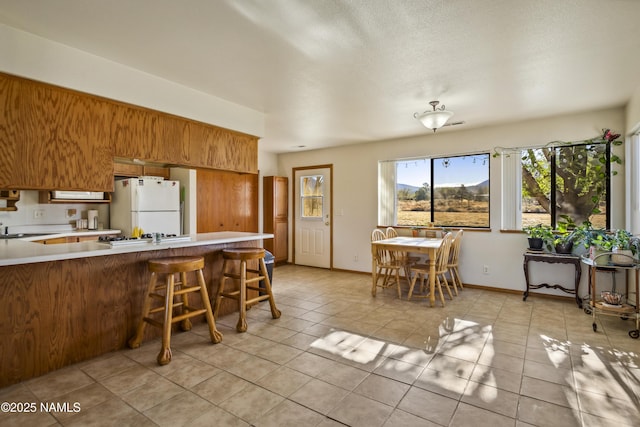 11280 N Zady Ln, Flagstaff, AZ 86004 - kitchen featuring light countertops, light tile patterned flooring, freestanding refrigerator, a peninsula, and brown cabinetry