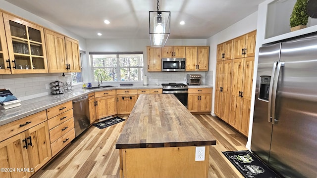 kitchen with a center island, appliances with stainless steel finishes, tasteful backsplash, decorative light fixtures, and wood counters