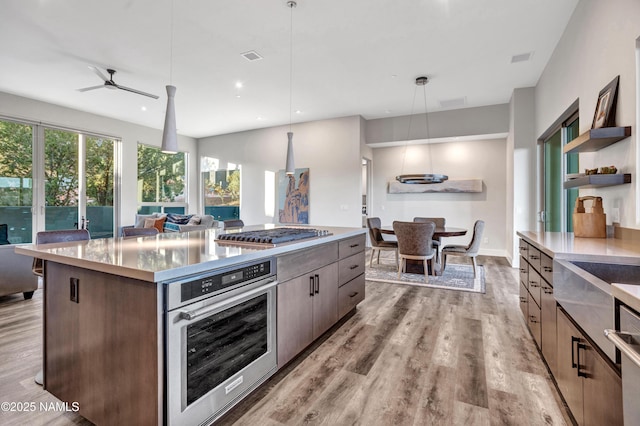 kitchen featuring open shelves, appliances with stainless steel finishes, a center island, open floor plan, and light wood-type flooring