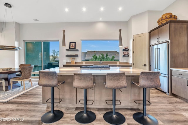 kitchen with light wood-style floors, a breakfast bar area, a kitchen island, high quality fridge, and light countertops