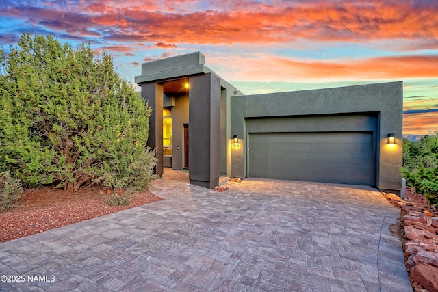 contemporary home with stucco siding, decorative driveway, and an attached garage
