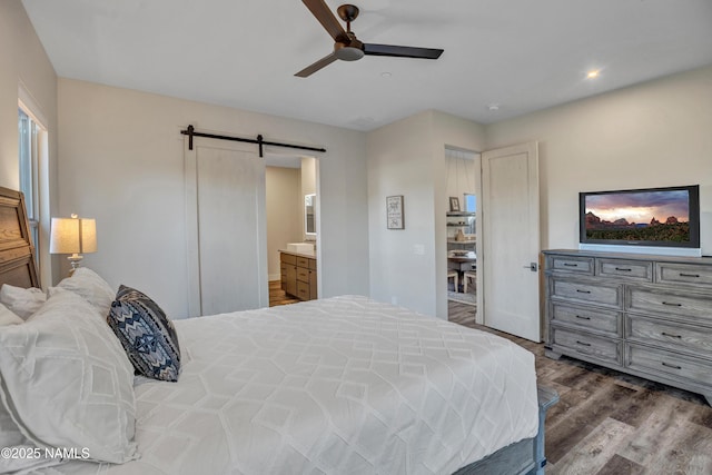 bedroom featuring a barn door, ensuite bathroom, recessed lighting, wood finished floors, and a ceiling fan