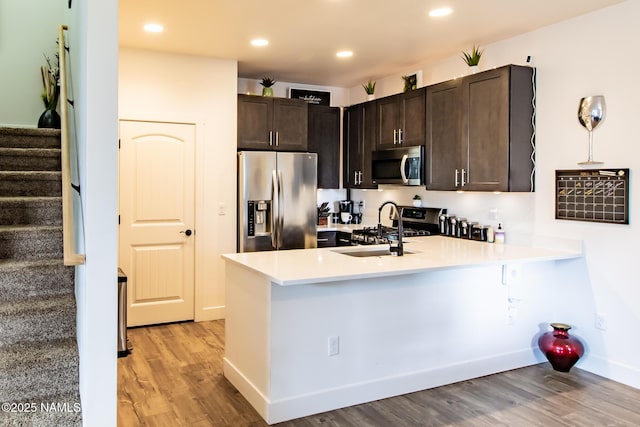 kitchen with dark brown cabinets, appliances with stainless steel finishes, a sink, light wood-style flooring, and a peninsula