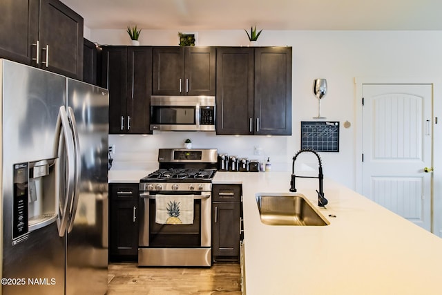 kitchen featuring appliances with stainless steel finishes, a sink, light wood finished floors, light countertops, and a peninsula