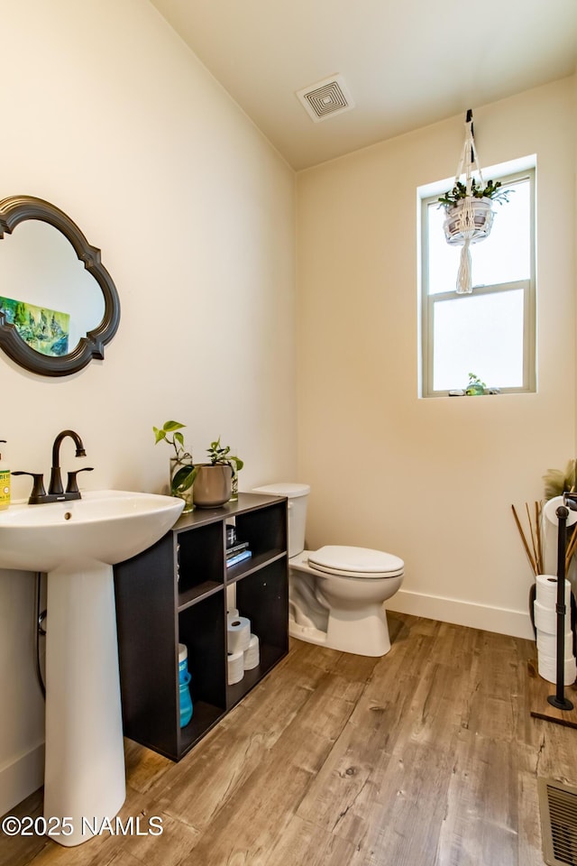 half bath featuring visible vents, baseboards, wood finished floors, and toilet
