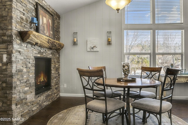 dining area featuring dark wood finished floors, a stone fireplace, baseboards, and a towering ceiling