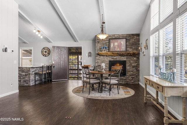 dining space featuring lofted ceiling with beams, plenty of natural light, a stone fireplace, and wood finished floors