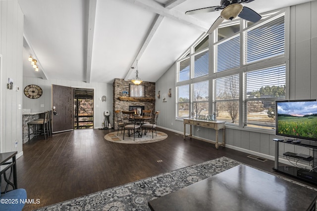 living area featuring wood finished floors, visible vents, ceiling fan, a stone fireplace, and beamed ceiling