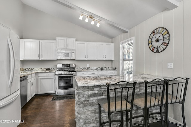 kitchen featuring lofted ceiling with beams, light stone counters, dark wood-type flooring, and appliances with stainless steel finishes