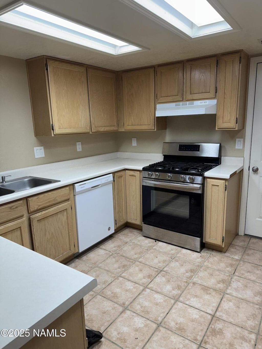 kitchen featuring stainless steel gas range oven, under cabinet range hood, a sink, white dishwasher, and light countertops