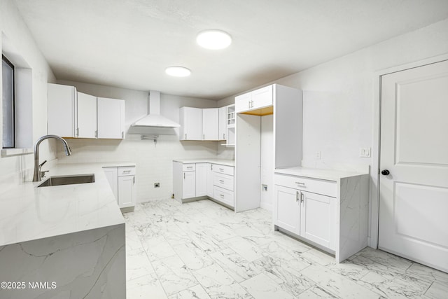 kitchen featuring light stone countertops, sink, wall chimney range hood, and white cabinets