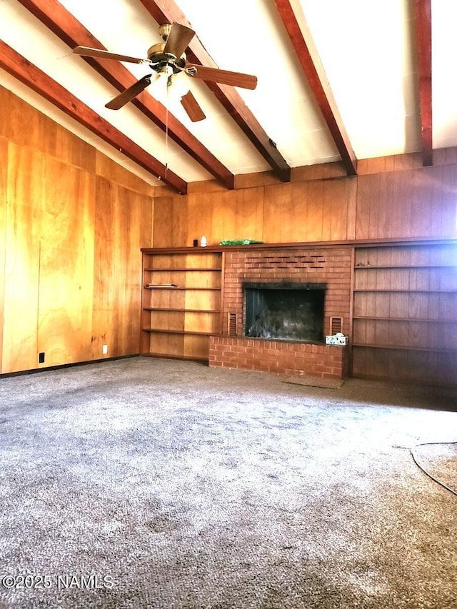 unfurnished living room with carpet, a ceiling fan, vaulted ceiling with beams, a fireplace, and wood walls