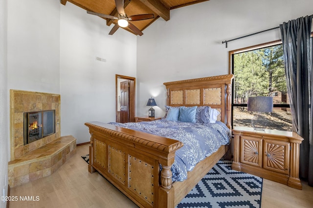 bedroom featuring high vaulted ceiling, a tile fireplace, visible vents, beam ceiling, and light wood finished floors