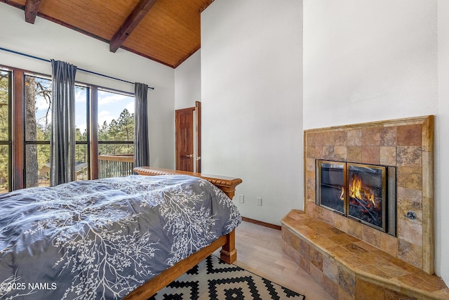 bedroom with high vaulted ceiling, a tile fireplace, wood ceiling, baseboards, and beamed ceiling