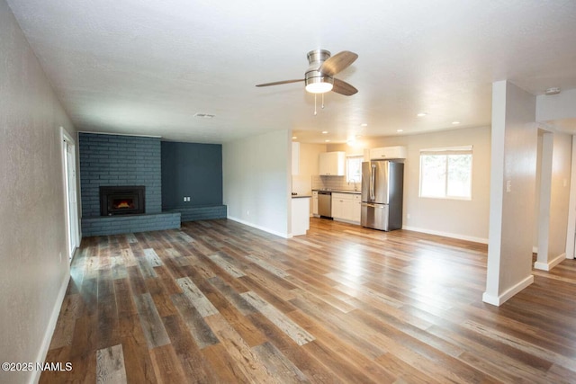 73 Seneca Dr, Flagstaff, AZ 86005 - unfurnished living room with a ceiling fan, a brick fireplace, baseboards, and light wood-style floors