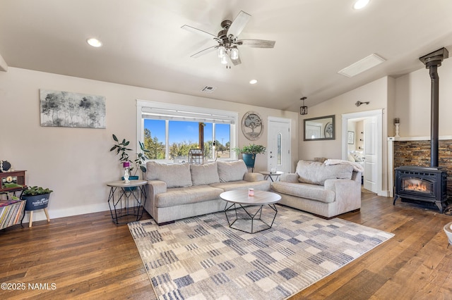 living room with ceiling fan, vaulted ceiling, wood-type flooring, and a wood stove