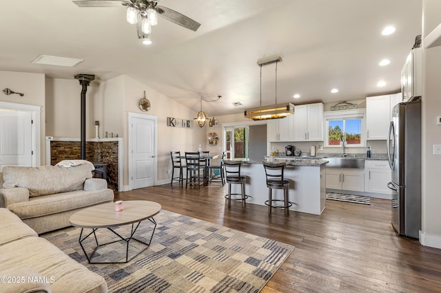 living room featuring sink, ceiling fan, dark hardwood / wood-style floors, vaulted ceiling, and a wood stove